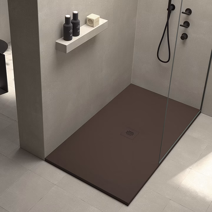 Modern shower with a dark brown base, glass partition, and a wall shelf holding black shampoo bottles and a bar of soap.