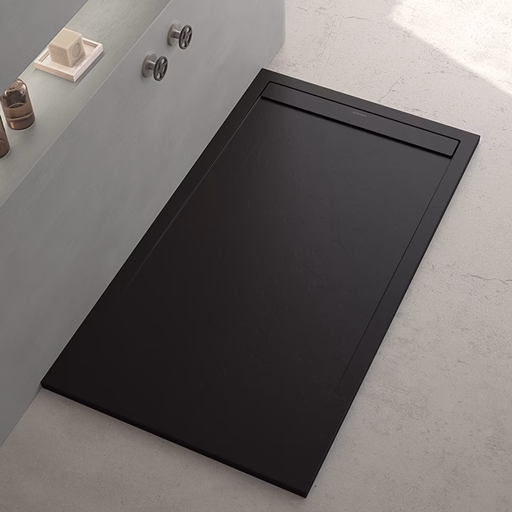Black rectangular floor access hatch in a modern bathroom beside a bathtub, with a slim handle slot along one edge for maintenance access.