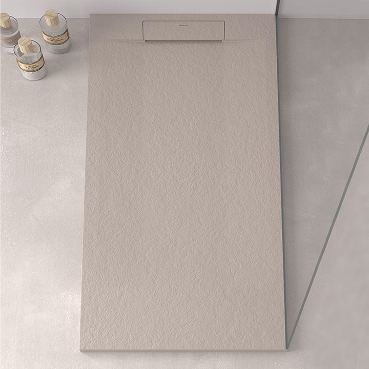 Beige textured bathroom panel with a slim recessed top handle, mounted beside a glass partition in a modern bathroom. A few small bottles sit on the counter to the left.