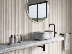 Contemporary bathroom scene with a round concrete-framed mirror above a marble sink and black faucet, beige vertical-tiled wall.