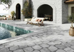 Poolside stone patio with a daybed, cushions, and a dining area under an arched stone doorway, overlooking the sea.