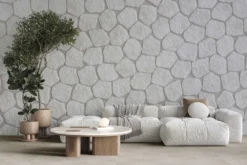 Living room with a light gray sofa, a soft blanket, and round wooden coffee table in front of a textured stone wall and potted plant.