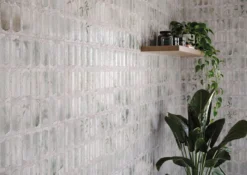 Geometric pink tile wall with a floating wooden shelf holding jars and an leafy green plant on the right side of the image.