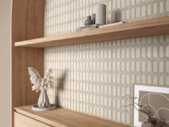 Wooden shelf display with a faceted ceramic vase, stacked books, and dried pampas grass against a pale geometric-tile wall.