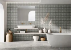 Modern bathroom with gray geometric tile wall, a white vessel sink on a concrete vanity, and brass fixtures. A mirror and decorative vases complete the scene.
