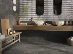 Spa-style bathroom with two rough stone vessel sinks on a wooden counter, brass taps, and a mosaic tiled wall.