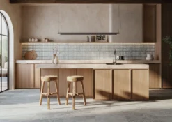 Modern kitchen with light wood cabinets, marble island, tiled backsplash, and three wooden bar stools.